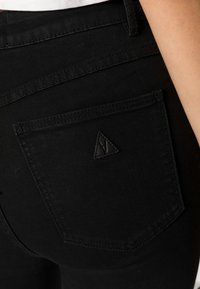 Jeans de mezclilla negra con un diseño ajustado, que presentan un único bolsillo trasero con un logo triangular y costuras tonalidades para un aspecto homogéneo.