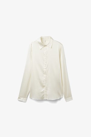 Lange Bluse in Cremefarbe mit klassischem Kragen, glatter Satintextur und Knopfleiste vorne. Leicht geschwungener Saum am unteren Ende.