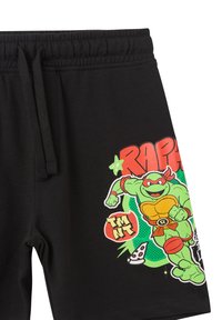 Pantaloni corti neri con una grafica colorata di un personaggio tartaruga verde con accenti rossi, testo "RAPHAEL" e dettaglio di una fetta di pizza. Materiale in cotone.