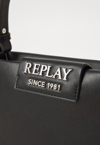 Zwarte leren tas met een zilveren logo plaat met "REPLAY" en "SINCE 1981," verfraaid met nette stiksels en een gestructureerd ontwerp.