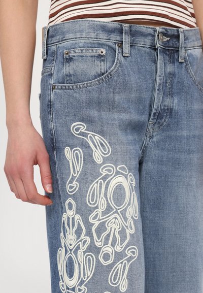 Light blue denim jeans featuring white abstract embroidery on the front, five pockets, and a buttoned waistband.