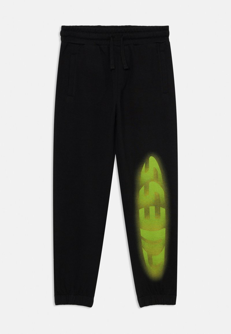 Pantalon de survêtement noir en mélange de coton, avec une taille élastique et des poignets élastiques, portant un grand logo "GUESS" dégradé vert sur la jambe gauche.