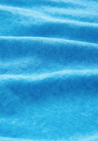 Tissu bleu à la texture lisse avec des motifs de tissage visibles, présentant des plis ondulants doux et une couleur vibrante et uniforme.