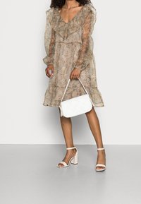 Robe en dentelle florale avec des détails froncés, assortie à un sac à main tissé blanc et des sandales à talons blocs beiges. Conception élégante, légère et aérienne.