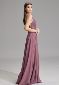 Robe longue violette avec un corsage ajusté en sequins et une jupe en chiffon fluide. Elle présente des bretelles fines et une silhouette drapée en douceur.