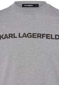 Grijze katoenen t-shirt met ronde hals en een opvallend zwart "KARL LAGERFELD" logo over de borst in een vetgedrukt, textuurachtig lettertype.