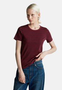 Burgundská pruhovaná tričko s krátkým rukávem, kulatým výstřihem a přiléhavým střihem, spárované s modrými džíny. Čistá, jednoduchá textilie.
