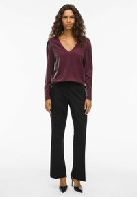 Burgunderfarget langermet topp med V-hals og glansfull tekstur, sammen med svarte vide bukser og svarte høye hæler. Enkel og elegant design.