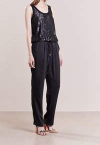 Top de tanque negro con lentejuelas, combinado con pantalones negros de corte suelto y cintura ajustable con cordón. La modelo lleva sandalias de tiras. Textura suave.