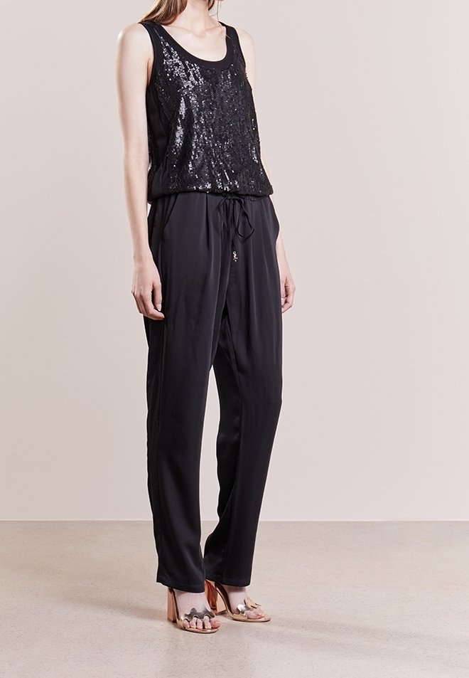 Top de tanque negro con lentejuelas, combinado con pantalones negros de corte suelto y cintura ajustable con cordón. La modelo lleva sandalias de tiras. Textura suave.
