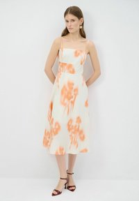 Hihaton midi-mekko kevyestä kankaasta, jossa on oranssi kukkakuvioinen tie-dye-kuviointi, istuva ykköspaita ja levenevä hame.