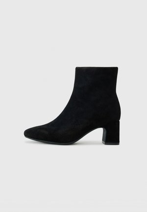 Bottines en suédine noire avec un bout pointu et un petit talon carré, présentant une texture lisse et un design minimaliste.
