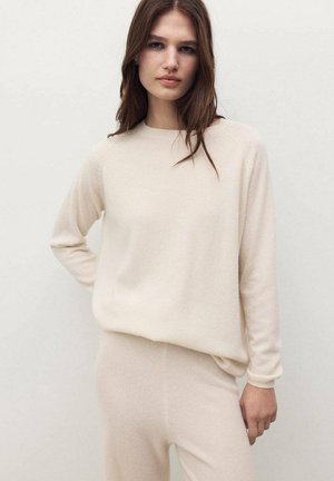 Sweater de punto beige con cuello redondo y manga larga, que presenta un corte relajado y una textura suave, combinado con leggings a juego.