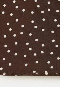 Tissu marron avec des petits pois blancs uniformément espacés et une couture visible le long du bord inférieur.