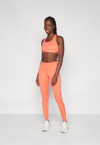 Nike sports-bh og tights i livlig korall. Elastisk materiale, tettsittende design, glatt tekstur, med logo-detaljer på begge produkter.