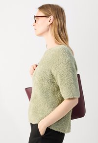 Fuzzy, light green short-sleeve sweater with a round neckline worn over black pants, paired with a burgundy handbag.