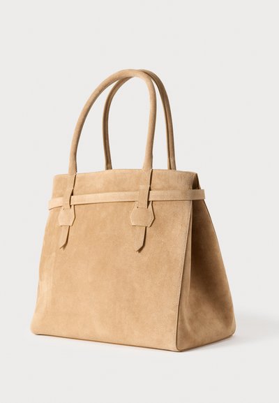 Τσάντα ώμου από μπεζ σουέτ με διπλές λαβές, γωνιώδη σχήμα και αντίθετη επίπεδη λωρίδα. Ομαλή υφή με ελάχιστες διακοσμήσεις.