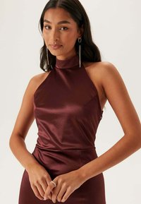 Vinröd halterneckklänning i slät satinväv. Figursydd siluett med minimal detaljering och en subtil glans.