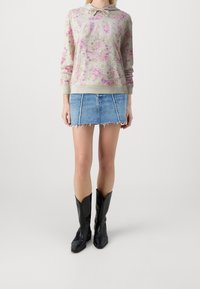 Sweater met bloemenpatroon in lichtbeige met roze accenten, voorzien van een capuchon en logo. Gecombineerd met een spijkerrok en zwarte cowboylaarzen.