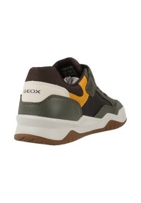 Scarpa sportiva Geox con una tomaia verde scuro e nera, accenti gialli, suola bianca e suola esterna in gomma marrone testurizzata. Logo visibile sul retro.
