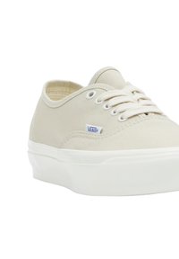 Sneaker in tela di un beige chiaro con suole in gomma bianche, punta rotonda, lacci che passano attraverso occhielli in metallo e un piccolo'etichetta blue Vans.