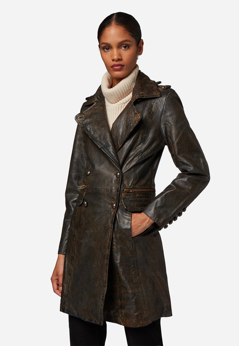 Brun läder trenchcoat med dubbelknäppning, slagkrage, knappdetaljer och sidofickor. Bärs över en krämfärgad polotröja.