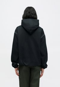 Μαύρο φαρδύ φούτερ με άνετη κουκούλα, εφαρμοστά μανσέτες και αντίθετη λευκή ραφή· συνδυασμένο με παντελόνι ελιάς.