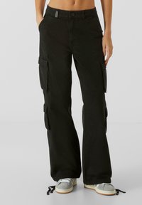 Pantalons cargo noirs avec une coupe décontractée, poches latérales et ourlets à cordon. Fabriqués en coton, avec une texture lisse et un matériel minimal.