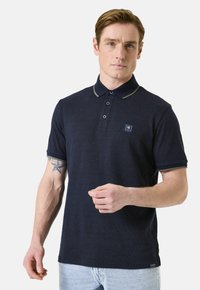 Polo marine avec un motif texturé subtil, col contrastant et bordures de manches, patte de boutonnage à trois boutons et petit écusson sur la poitrine.