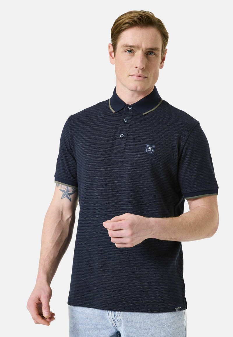 Polo marine avec un motif texturé subtil, col contrastant et bordures de manches, patte de boutonnage à trois boutons et petit écusson sur la poitrine.