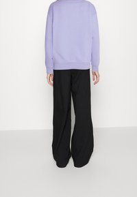 Sudadera lila con hombros caídos, combinada con pantalones amplios negros. Tejido suave, diseño sencillo y corte relajado. Sin patrones visibles.