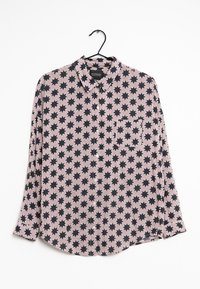 Chemise à manches longues noire et rose avec un motif d'étoiles répétées, col boutonné, et une légère courbe à l'ourlet, fabriquée en tissu léger.