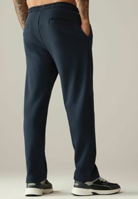 Pantalones de chándal azul marino de corte relajado, con cintura elástica y dos bolsillos traseros. Combinados con zapatillas deportivas negras y grises.