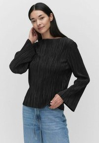 Sort plisset top med bådhals og lange klokkeærmer, parret med lyseblå jeans. Stoffet har et struktureret stribe mønster.
