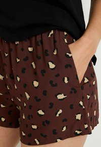 Shorts marron avec un imprimé léopard noir et beige, dotés d'une taille élastique et de poches latérales, fabriqués en tissu doux et léger.