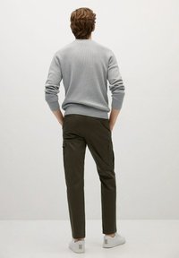 Grau gerippter Pullover, olivgrüne Cargo-Hosen mit Seitentaschen und weiße Sneaker mit einem Rückenelement. Rückansicht vor einem neutralen Hintergrund.