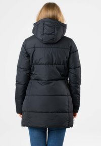 Schwarze Pufferjacke mit Kapuze und steppgenähten Paneelen. Sie hat eine taillierte Taille und einen mittellangen Schnitt, kombiniert mit blauen Jeans.
