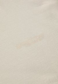 Beige katoenstof met een subtiele textuur en een geprinte logo in een iets donkere tint. Glad oppervlak zonder zichtbare patronen.