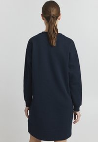 Mörkblå sweatshirtklänning i mjuk bomullsblandning, med långa ärmar, ribbade muddarna och en avslappnad silhuett, med en något rundad nederkant.
