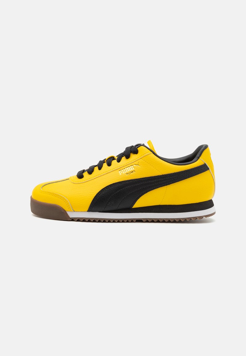 Dzelteni ādas sneakers ar melniem akcentiem, teksturēta virsma, melni šņorējamie auklas un brūna gumijas zole. Sānu profils.