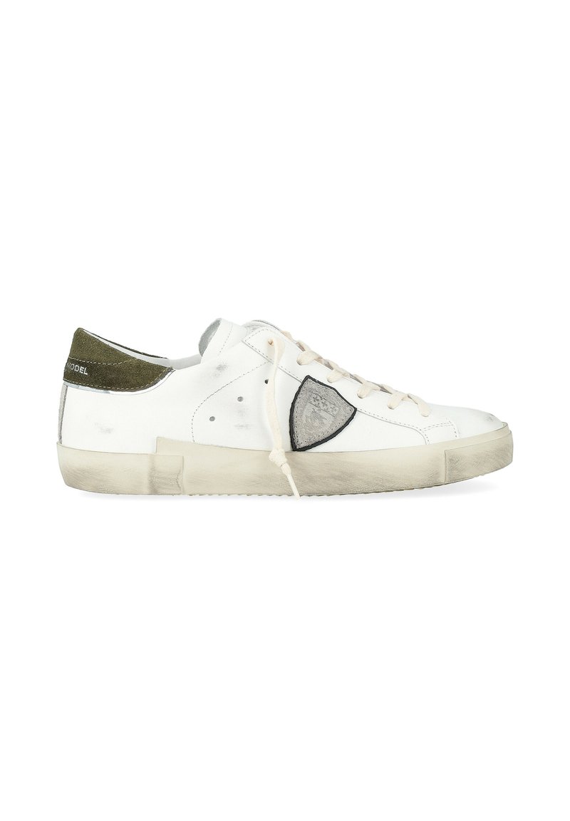 Zapatilla baja blanca con talón de ante verde, logo en forma de escudo gris en el costado, cordones color blanco sucio y suela de goma desgastada.
