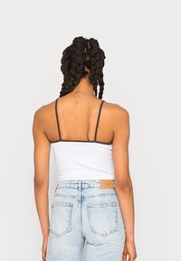 Top branco de alças finas com detalhes castanhos, combinado com jeans de cintura alta em azul claro, apresentando um corte clássico e um acabamento desbotado.