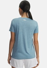 Helles blaues Sport-T-Shirt mit glatter Textur, kurzen Ärmeln und einem kleinen Logo am Hals. Kombiniert mit weißen Mesh-Shorts.