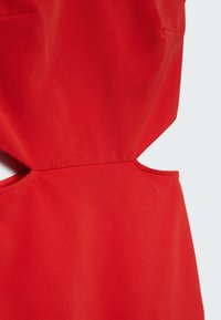 Robe en tissu rouge présentant un design épuré, avec une découpe sur le côté et des coutures plates. Texture lisse sans éléments métalliques apparents ni motifs.