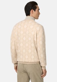 Pull en beige à motifs avec un col montant, présentant des motifs en diamant et des poignets et un ourlet côtelés. Fabriqué à partir d'un tissu doux et texturé.