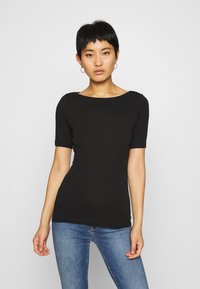 Musta lyhythihainen t-paita venepääntiellä, sileä pinta ja slim fit -muotoilu; yhdistetty sinisiin farkkuihin. Yksinkertainen, ilman näkyviä kuvioita tai koristeita.