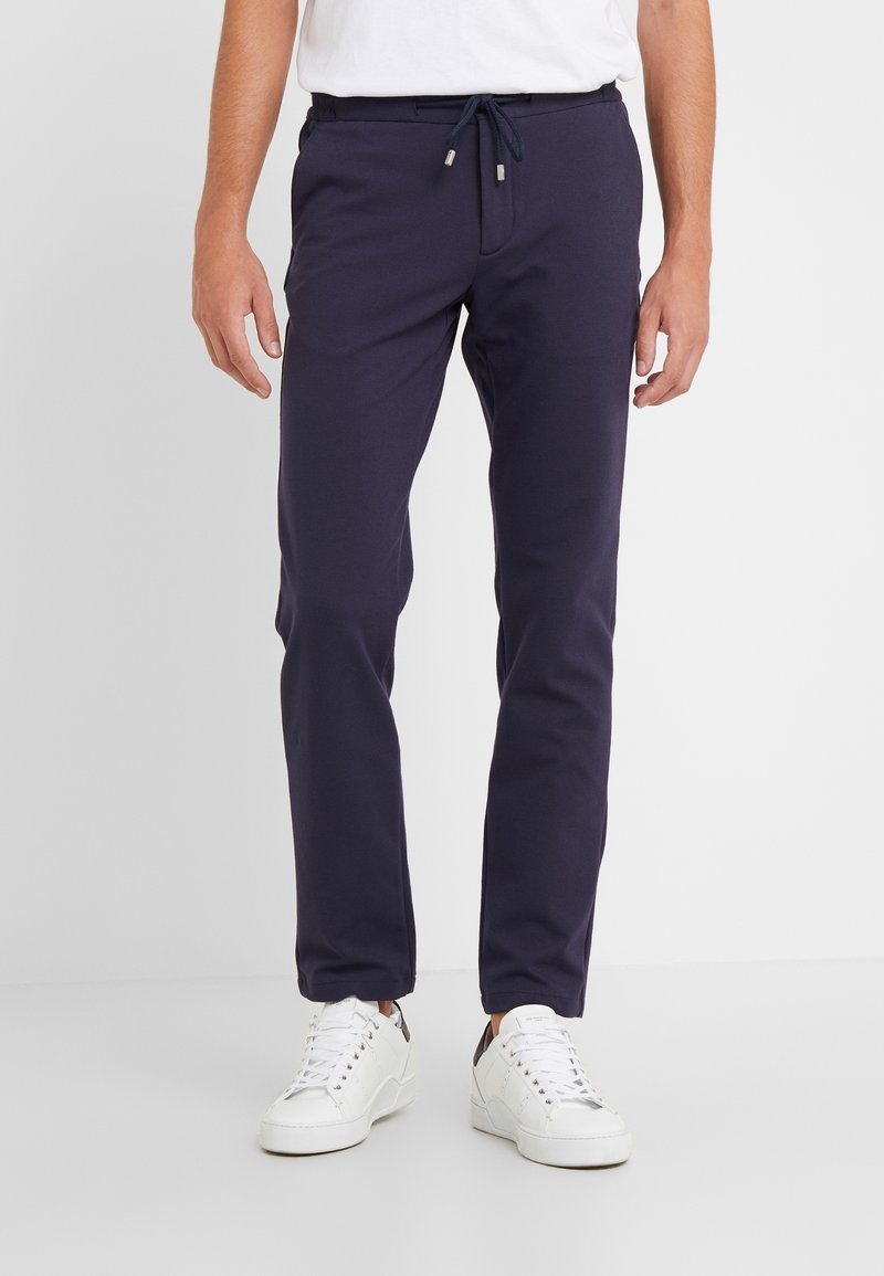 Marineblå joggerbukser med elastisk talje og justerbar snor, lavet af blødt materiale, med sidelommer og en slim fit-design.