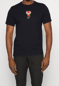 Svart bomulls t-shirt med en grafisk design av en orange och vit tiger samt en liten vit Nike-logotyp på framsidan. Korta ärmar.