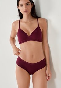 Burgundowa bielizna składająca się z biustonosza i majtek, wykonana z miękkiego, elastycznego materiału z trójkątnym fasonem miseczek i delikatnym wykończeniem. Prosty, bezszwowy kształt.