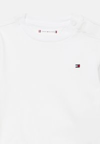 Λευκή βαμβακερή φανέλα με πλεκτό λαιμό, με μικρή κεντημένη λογότυπο Tommy Hilfiger σε κόκκινο και μπλε χρώμα στο αριστερό στήθος.